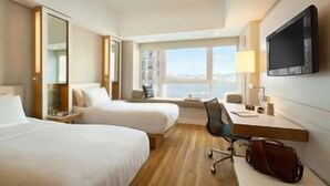 Une chambre d’hôtel avec deux lits, un bureau, une chaise, une télévision et une fenêtre donnant sur un paysage agréable.