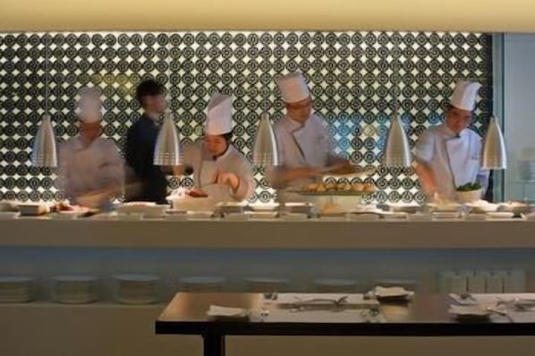 A kitchen with chefs in white uniforms, a patterned wall, and a buffet setup.