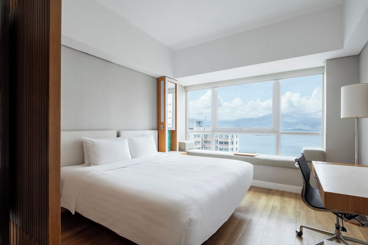 Ein Hotelzimmer mit einem großen Bett, einem Schreibtisch und einem Fenster mit Blick auf die Stadt.
