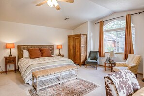Ein Schlafzimmer mit einem Bett, Nachttischen, einem Holzschrank, einem Sessel, einer Bank, einem Teppich und einem Fenster mit Vorhängen.