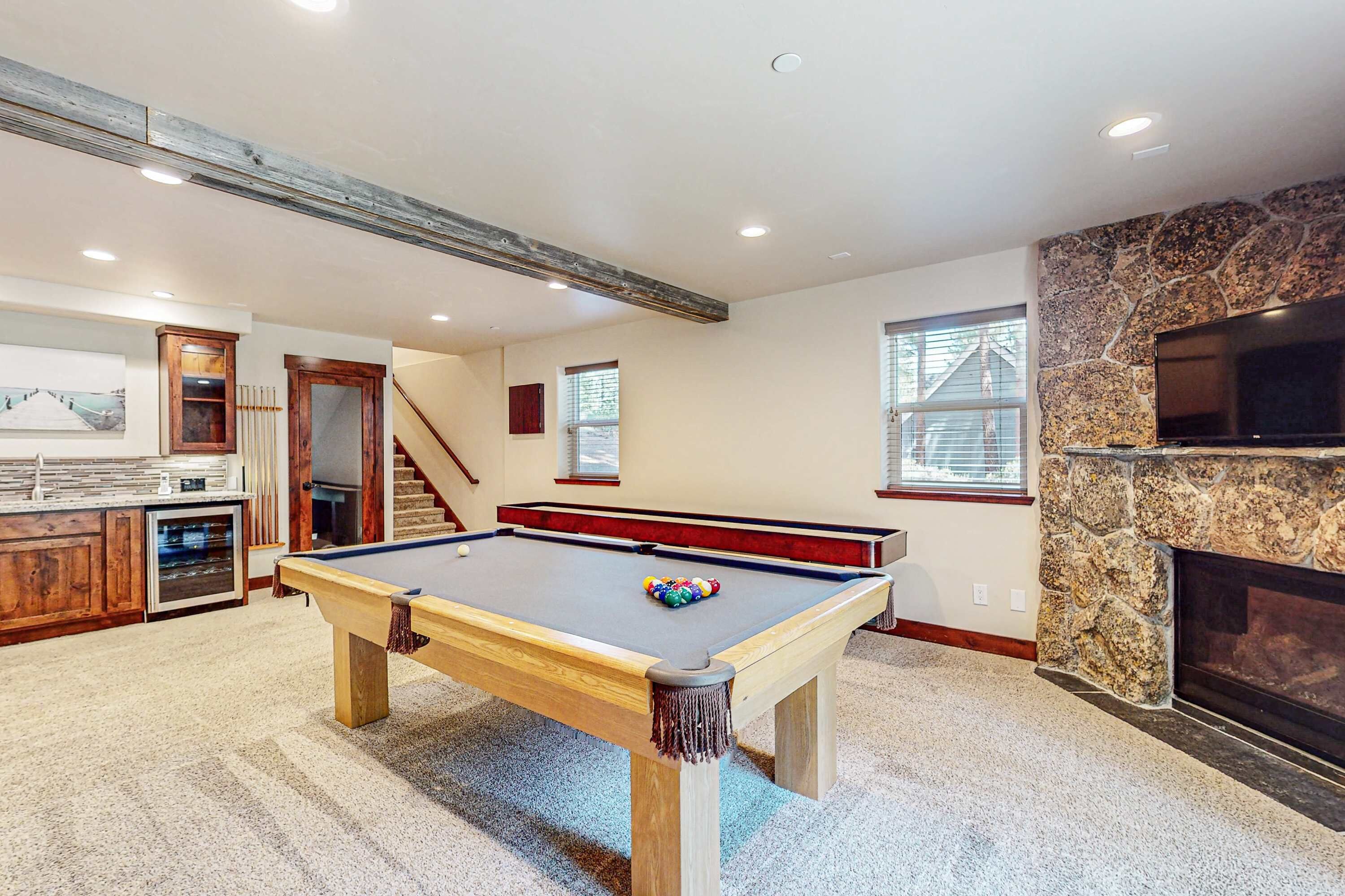 A pool table in a room with a stone fireplace, wooden cabinets, and a staircase.
