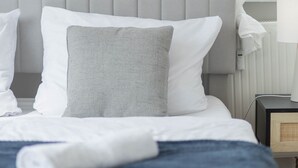 Un lit bien fait, avec une tête de lit grise, des oreillers blancs et une couverture bleue.