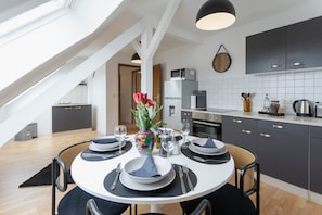 Una cocina moderna con armarios oscuros, un salpicadero blanco de azulejos y una zona de comedor con una mesa redonda para cuatro comensales.