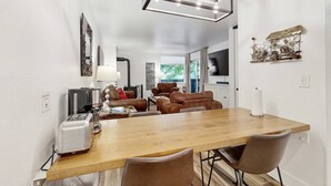 Une cuisine moderne avec une table en bois, des chaises en cuir marron, une machine à café et un téléviseur fixé au mur.