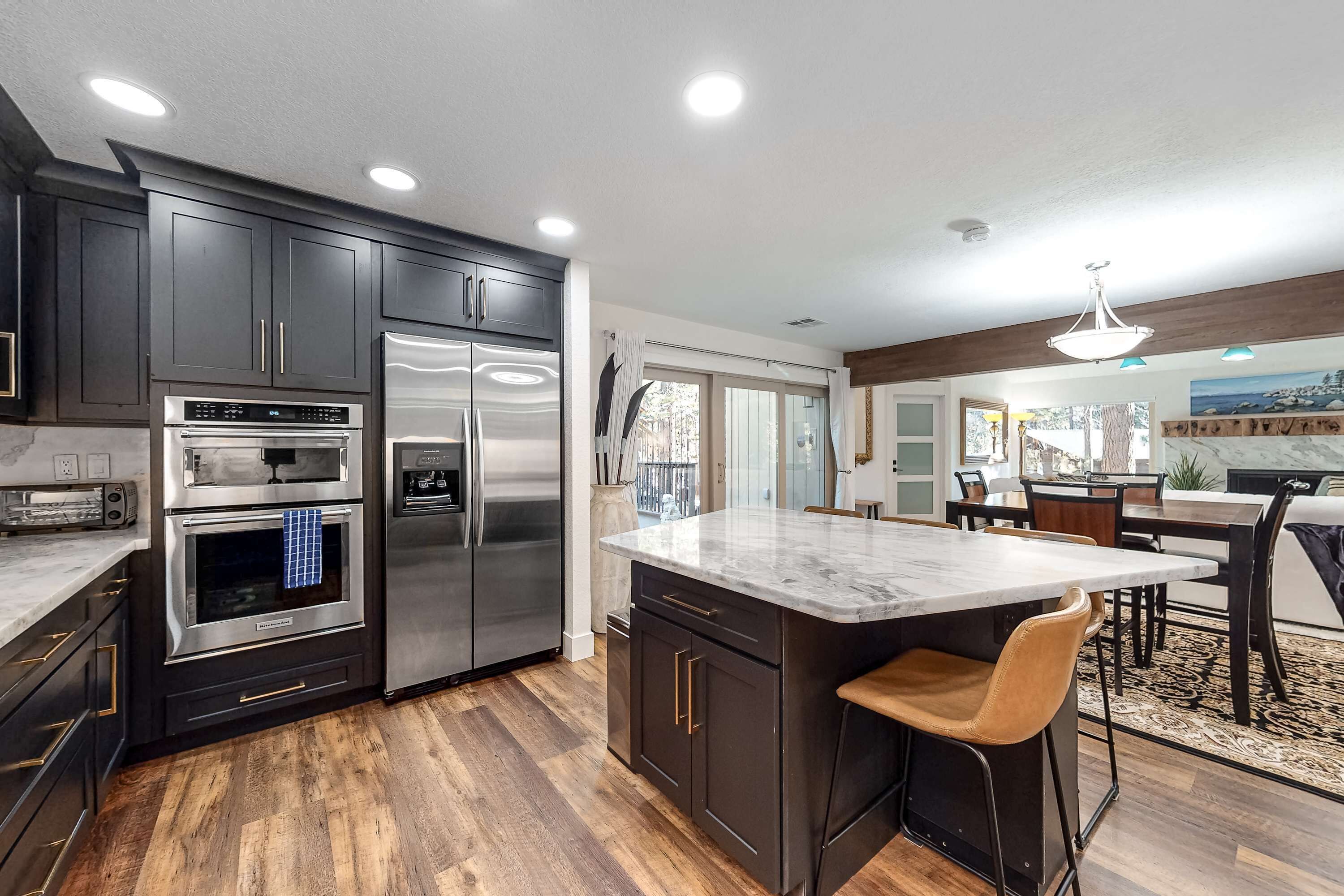 A modern kitchen with dark cabinetry, stainless steel appliances, and a marble island.