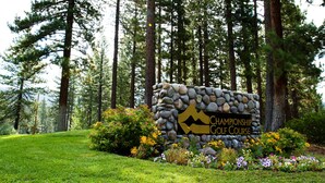 Ein Steinschild mit der Aufschrift 'CHAMPIONSHIP GOLF COURSE', umgeben von einer gepflegten Rasenfläche und verschiedenen blühenden Pflanzen.