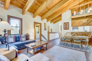 Un salón amplio con techo de madera, un sofá, una mesa de comedor con sillas y una escalera que lleva a un nivel superior.