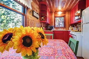 Ein Interieur einer Holzhütte mit Küche, Essbereich und einem Fenster mit Blick auf Bäume.