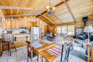 A wooden cabin interior with a kitchen, dining area, and fireplace. - Mountain home with wood stove, W&D, & propane heat - near lifts & trails (Truckee)