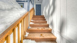 Eine Holztreppe führt zu einer blauen Tür, umgeben von Schnee.