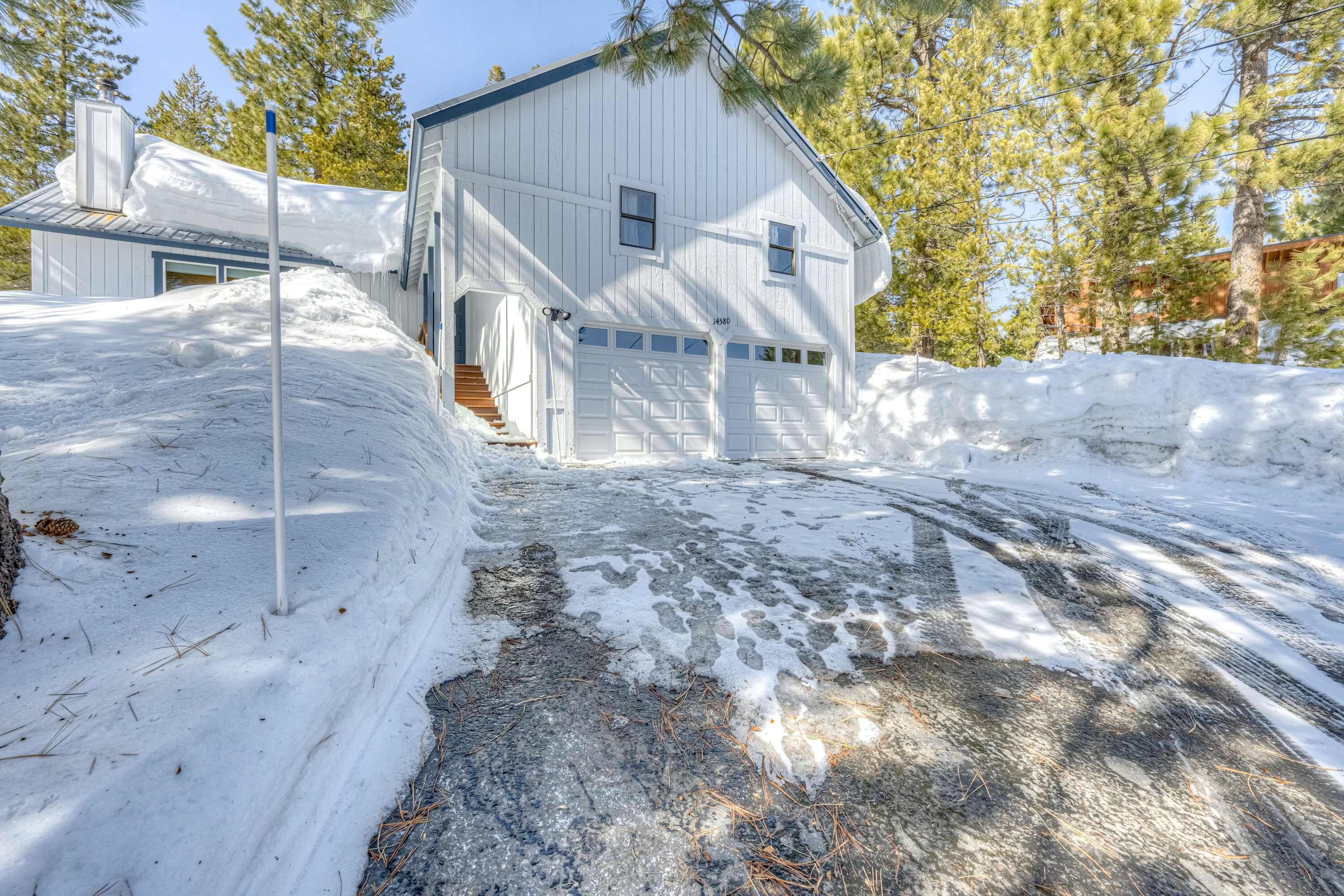 A white two-story house with a garage, surrounded by snow and trees.