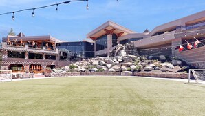 Ein Hotel mit moderner Architektur, eine angelegte Grünfläche mit Felsen und einem kleinen Wasserfall sowie Sitzmöglichkeiten im Freien.