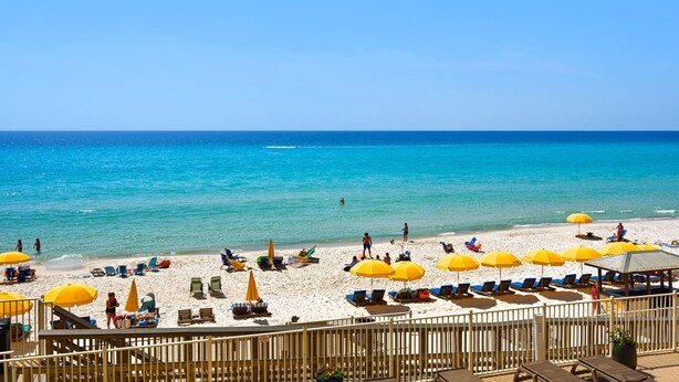 Una playa con sombrillas, sillas de descanso y una terraza de madera con vista al océano.