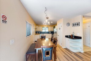 A dining area with a table, chairs, a kitchen in the background, a 'No Smoking' sign, and a clock on the wall.