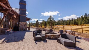 Un espace patio avec des sièges d’extérieur, une cheminée en pierre et un bâtiment en bois doté de grandes fenêtres.