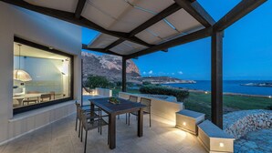 A covered outdoor dining area with a table and chairs, a view of the sea, and a mountainous landscape in the background. - Beautiful private villa for 12 people with WIFI, A/C, TV and patio (Favignana)