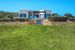 Une maison moderne à deux étages, dotée d’un mur en pierre et d’une pelouse verdoyante à l’avant.