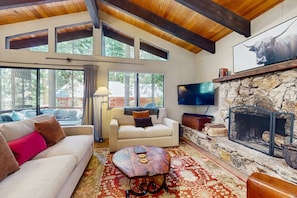 A cozy living room with a stone fireplace, a sofa, a coffee table, and a television mounted on the wall.