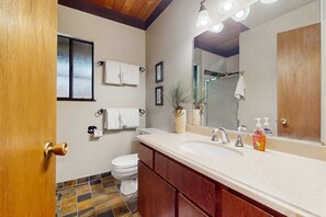 A bathroom with a toilet, a sink with a mirror, and a shower area. - Rustic, comfy, dog-friendly cabin in the pines - walk to homeowners lake & beach (Homewood)