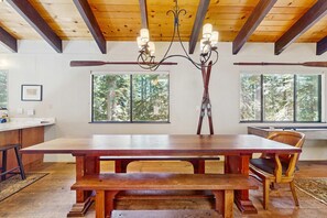 A dining area with a wooden table, benches, and a chandelier. There are windows with a view of trees. - Rustic, comfy, dog-friendly cabin in the pines - walk to homeowners lake & beach (Homewood)