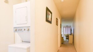 A laundry room with a washer and dryer, a hallway leading to a dining area, and a door at the end. - Ocean Block, 1 Bedroom Condo, WiFi, Washer/Dryer, 2 Blocks to Seacrets (Ocean City)