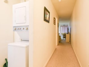 A laundry room with a washer and dryer, a hallway leading to a dining area, and a door at the end. - Ocean Block, 1 Bedroom Condo, WiFi, Washer/Dryer, 2 Blocks to Seacrets (Ocean City)