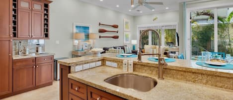 A kitchen with granite countertops, a stainless steel sink, wooden cabinets, and a dining area with a view of the outdoors.