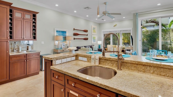 A kitchen with granite countertops, a stainless steel sink, wooden cabinets, and a dining area with a view of the outdoors. - **THE ELEGANT EGRET @ OLD TOWN** Home & Pool + Last Key White Glove Service... (Key West)