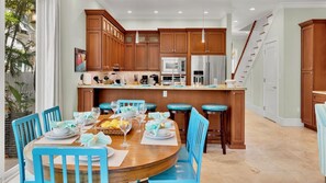 Een moderne keuken met houten kastjes, een centraal eiland en een eethoek met blauwe stoelen en een ronde tafel voor zes personen.