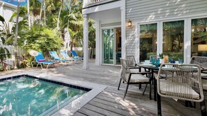 Ein Poolbereich mit Liegestühlen, einem Esstisch mit Stühlen und einer überdachten Terrasse.