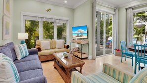 A living room with a sofa, armchairs, a coffee table, and a television. There is a sliding glass door leading to an outdoor area with a pool and lounge chairs. - **THE ELEGANT EGRET @ OLD TOWN** Home & Pool + Last Key White Glove Service... (Key West)