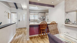 An open-plan living area with a kitchen, wooden flooring, and a dining table with chairs. - Updated mountain condo with pool access & wood fireplace - near skiing (Incline Village)