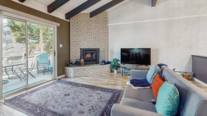 A living room with a fireplace, a sofa, a television, and a sliding glass door leading to an outdoor area. - Updated mountain condo with pool access & wood fireplace - near skiing (Incline Village)