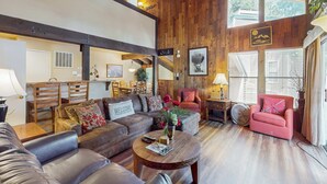 Un salon spacieux avec un plafond haut, des poutres apparentes, un ensemble de canapés, une table basse et un fauteuil rouge.