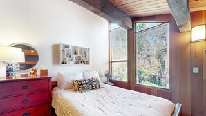 Een slaapkamer met een bed, een kaptafel, een spiegel, een plank met decoratieve objecten en een raam met jaloezieën.