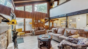 A spacious living area with wooden walls, a high ceiling, and large windows. There are two sofas, a coffee table, and a fireplace. - Your next vacation getaway is less than 200 steps to a private beach on the lake (South Lake Tahoe)