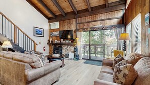 A spacious living room with a fireplace, wooden ceiling beams, and a large window overlooking a deck. - Your next vacation getaway is less than 200 steps to a private beach on the lake (South Lake Tahoe)