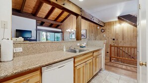 A kitchen with wooden beams, granite countertop, white dishwasher, and wooden cabinets. - Get to know the great outdoors from this 3-story home with lakefront pool access (South Lake Tahoe)
