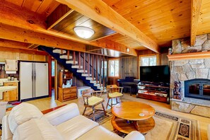 A wooden interior with a sofa, chairs, a TV, a fireplace, and a staircase. - Two-story cabin with a wood fireplace, washer&dryer, & decks (Tahoe City)