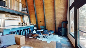 A cozy cabin interior with a loft bedroom, a kitchen area, and a seating area with a fireplace. - Woodland home in quiet location with deck, fireplace & entertainment options (Kings Beach)