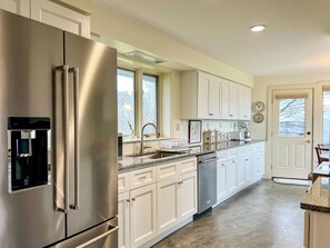 A modern kitchen with stainless steel appliances, white cabinetry, a built-in water dispenser, and a large window providing natural light. - Morning Mist: 3  BR, 2.5  BA House in Harpswell, Sleeps 6 (Harpswell)