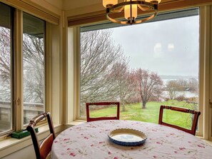 A room with a table and chairs facing a large window overlooking a grassy area and a body of water. - Morning Mist: 3  BR, 2.5  BA House in Harpswell, Sleeps 6 (Harpswell)