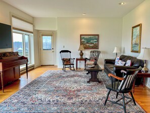 A living room with a piano, a patterned rug, a rocking chair, a sofa, and a painting on the wall. - Morning Mist: 3  BR, 2.5  BA House in Harpswell, Sleeps 6 (Harpswell)