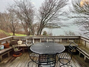 A wooden deck with a round metal table and chairs, surrounded by potted plants and a bench. - Morning Mist: 3  BR, 2.5  BA House in Harpswell, Sleeps 6 (Harpswell)