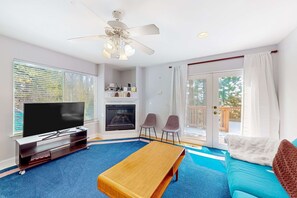 Een woonkamer met een televisie, open haard, twee stoelen, een tafel en een bank.
