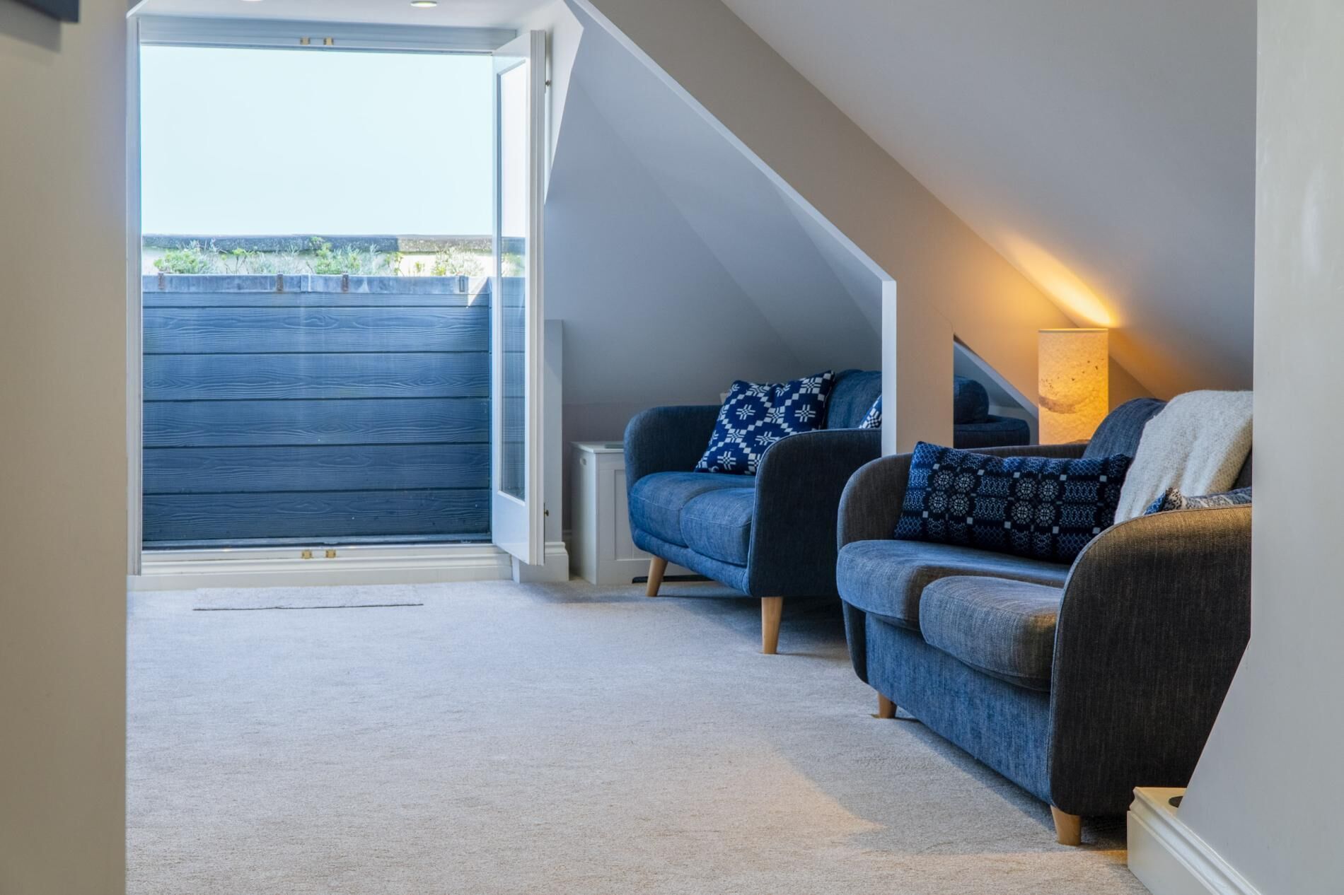 Une chambre aménagée en mezzanine avec une grande fenêtre, deux canapés, un téléviseur et une lampe.