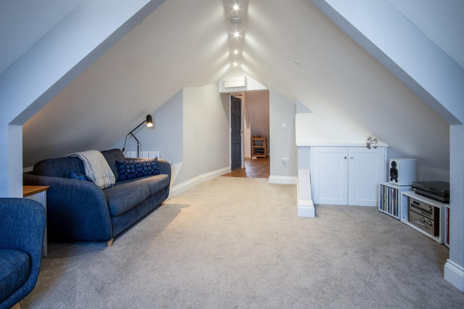 Une pièce de style loft avec un plafond en pente, un canapé, un bureau et un meuble contenant du matériel audio.
