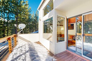 Una casa moderna con terraza de madera, antena parabólica y puerta de cristal que da a un espacio de estar con sofá y lámpara.