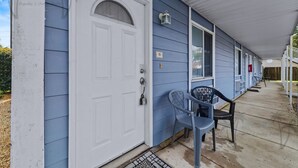 A building with a white door, a blue exterior, and a covered porch with chairs. - Oak Shores Studio 13 | Just a Short Walk to the Beach! (Biloxi)