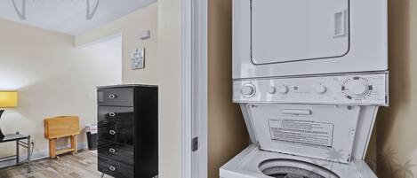 A laundry area with a washing machine, a black cabinet, and a wooden stool.